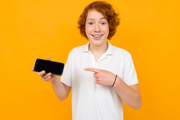 Caucasian guy in a white shirt with a smartphone with a blank template on a yellow background with copy space