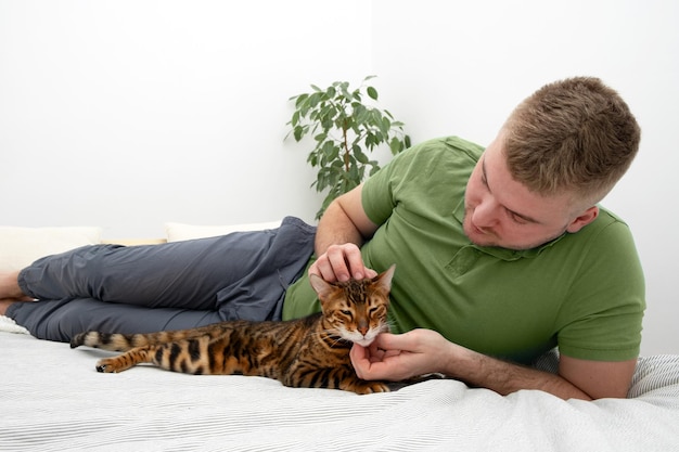 Caucasian handsome blond bearded man caressingstroking beautiful bengal catPeople and pet relationshiplovecareAnimal and person friendshipRelaxing at home conceptLifestyle