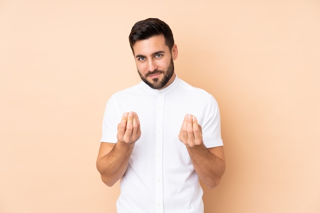 Caucasian handsome man on beige wall making money gesture