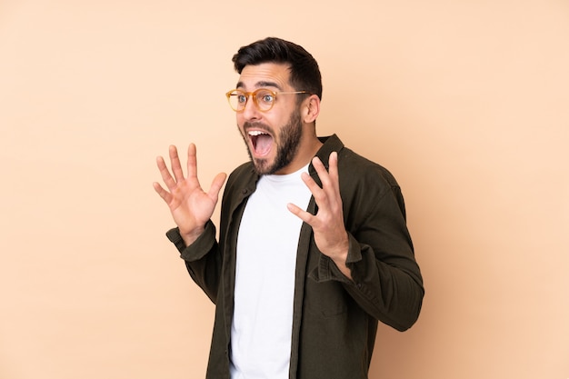 Caucasian handsome man on beige wall with surprised facial expression