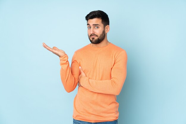 Caucasian handsome man having doubts over blue wall