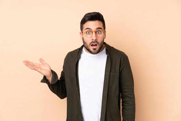 Caucasian handsome man isolated on beige wall making doubts gesture