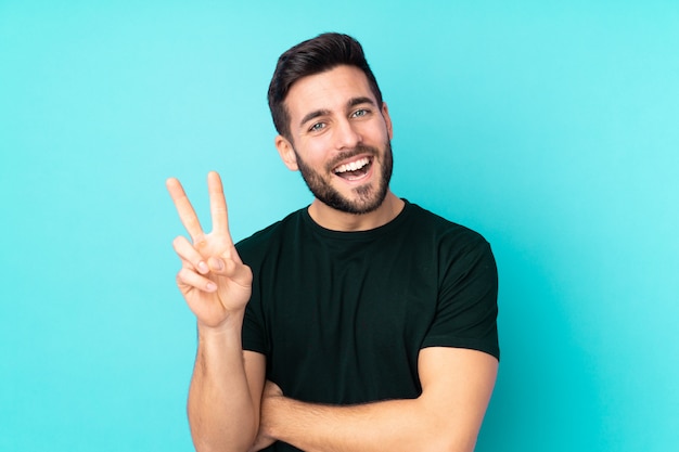 Caucasian handsome man isolated on blue wall smiling and showing victory sign