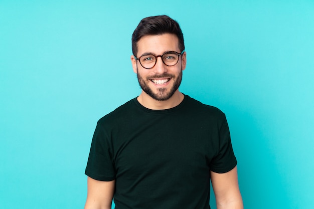 Caucasian handsome man isolated on blue wall with glasses and happy