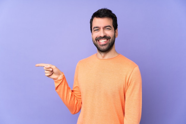 Caucasian handsome man over isolated purple space pointing finger to the side