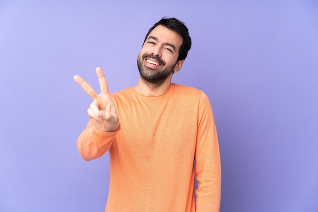 Caucasian handsome man over isolated purple space smiling and showing victory sign