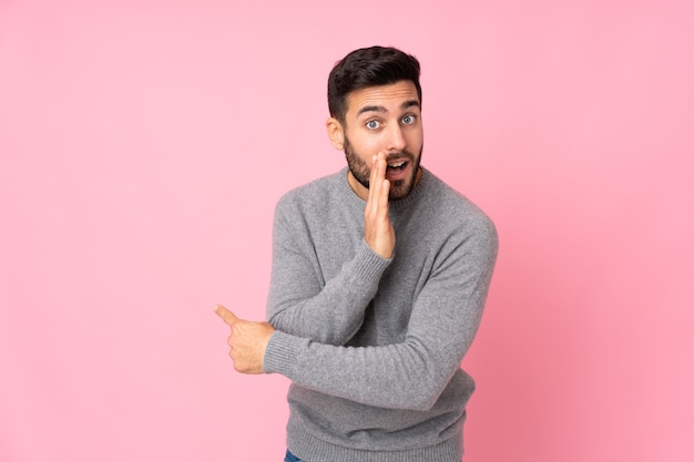 Caucasian handsome man over isolated wall pointing to the side to present a product and whispering something