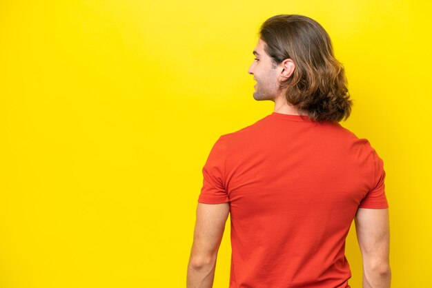 Caucasian handsome man isolated on yellow background in back position and looking side