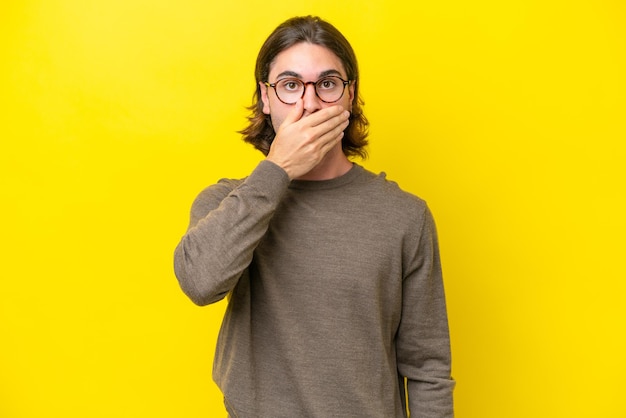 Caucasian handsome man isolated on yellow background covering mouth with hand