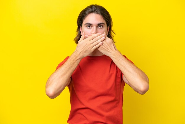 Caucasian handsome man isolated on yellow background covering mouth with hands