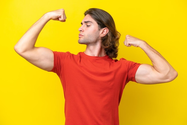 Caucasian handsome man isolated on yellow background doing strong gesture