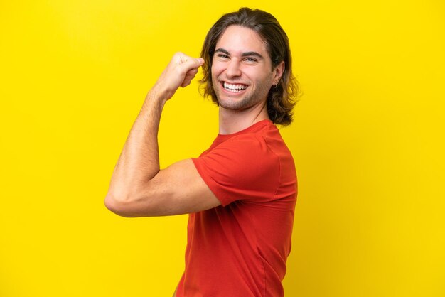 Caucasian handsome man isolated on yellow background doing strong gesture