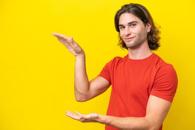 Caucasian handsome man isolated on yellow background holding copyspace to insert an ad