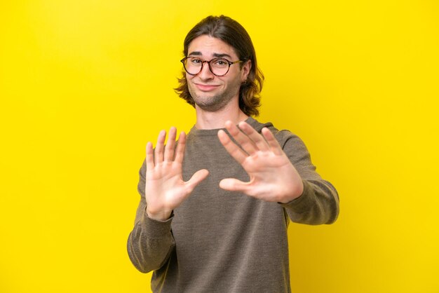 Caucasian handsome man isolated on yellow background nervous stretching hands to the front