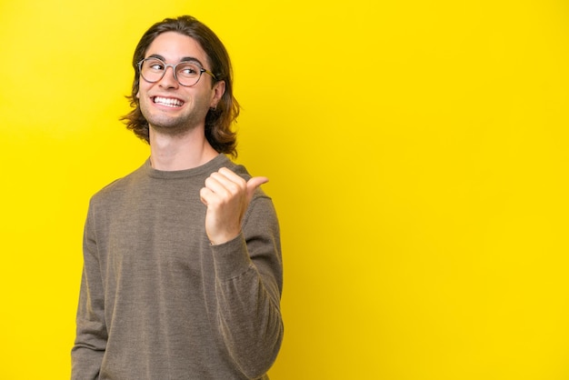 Caucasian handsome man isolated on yellow background pointing to the side to present a product