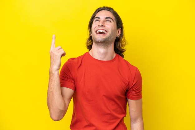 Caucasian handsome man isolated on yellow background pointing up and surprised