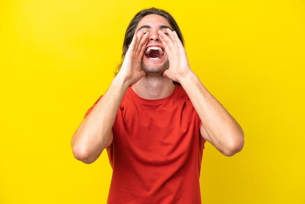 Caucasian handsome man isolated on yellow background shouting and announcing something