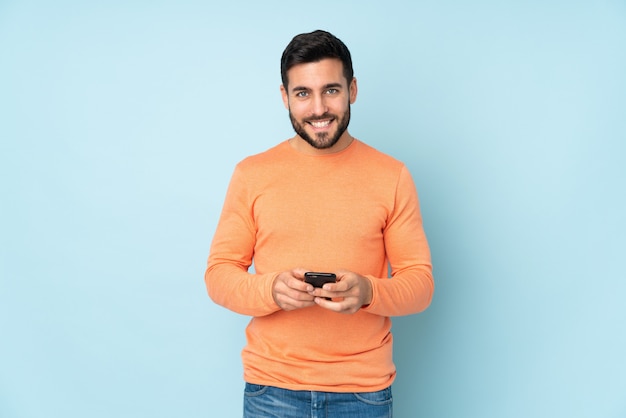 Caucasian handsome man sending a message with the mobile over blue wall