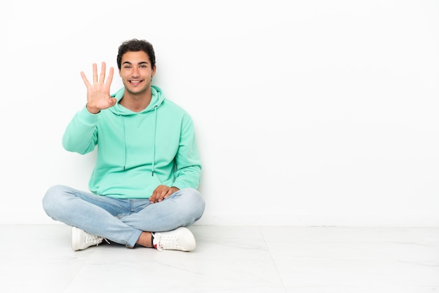 Caucasian handsome man sitting on the floor happy and counting four with fingers