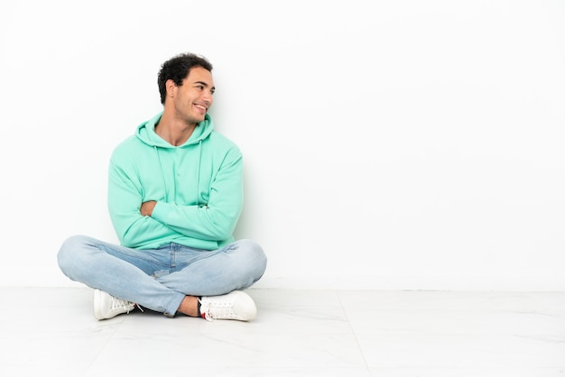 Caucasian handsome man sitting on the floor looking side