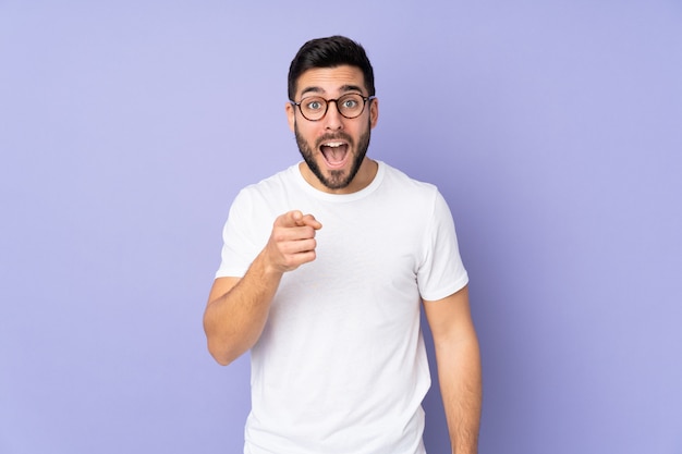 Caucasian handsome man over wall surprised and pointing front