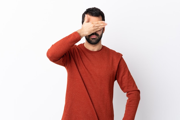 Caucasian handsome man with beard over white covering eyes by hands. Do not want to see something