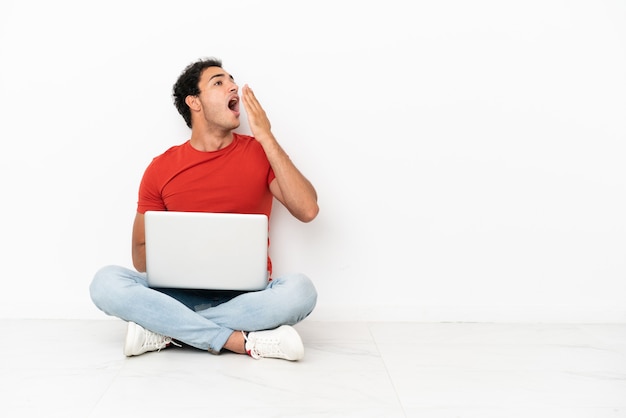 Caucasian handsome man with a laptop sitting on the floor yawning and covering wide open mouth with hand