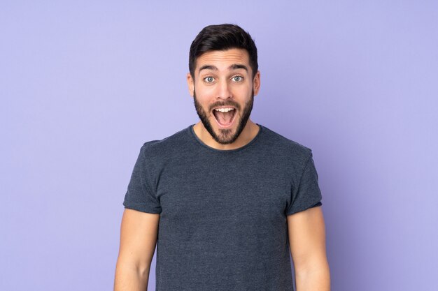 Caucasian handsome man with surprise facial expression over purple wall