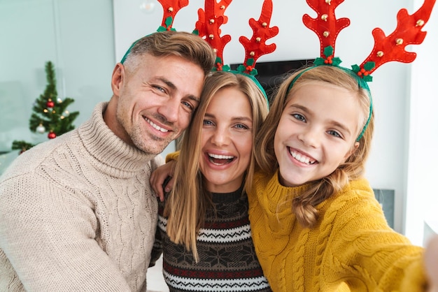 Foto famiglia felice caucasica in corna di renna di natale che celebrano le vacanze a casa con l'albero di capodanno