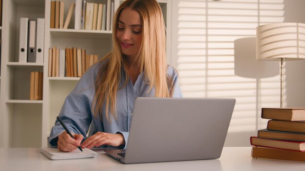 Caucasian happy female student girl at home library studying online with books laptop distant