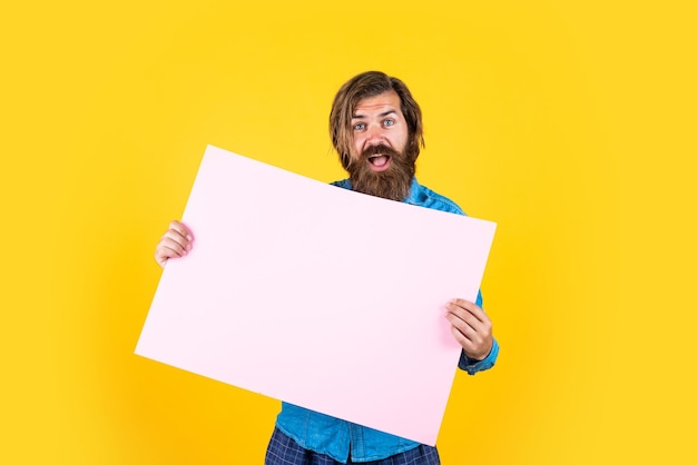 I pantaloni a vita bassa caucasici con la barba e i capelli alla moda tengono un banner di carta con l'annuncio dello spazio di copia