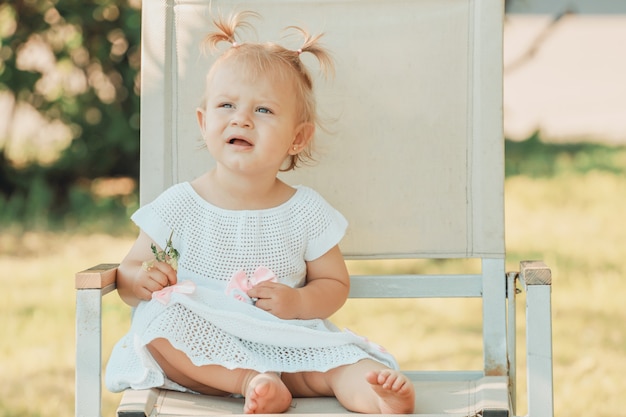 写真 夏に庭の椅子に座っている白人の幼児の女の子のブロンド。高品質の写真