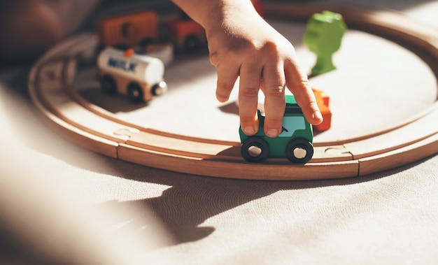 Caucasian kid is playing with toy train on the railway on the floor