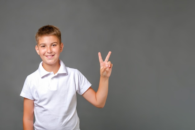 Caucasian kid standing over isolated grey background and showing victory sign