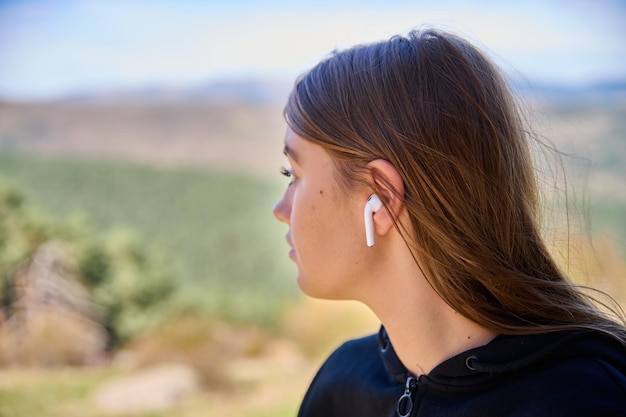 Caucasian lady listening to music and typing on her phone with the green hills on the background