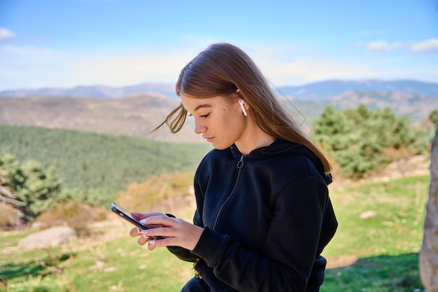 音楽を聴いて、背景に緑の丘と彼女の携帯電話で入力する白人女性