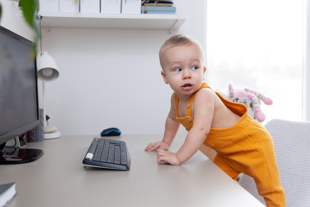 Photo caucasian little baby boy with funny facial expression try to exploring computer, monitor and keyboard,