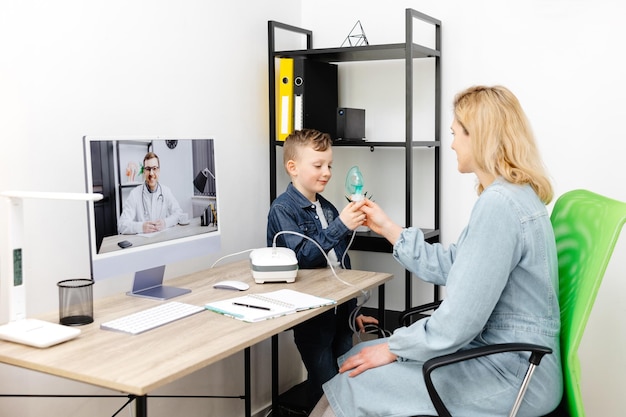 Caucasian little boy making inhalation with nebulizer at home A young mother helping her son to inhale with a nebulizer at an online meeting with a doctor