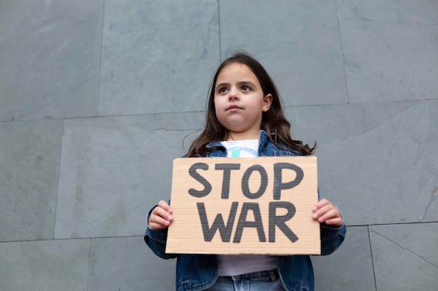 Кавказская маленькая девочка протестует против войны Она идет по улице с табличкой ручной работы