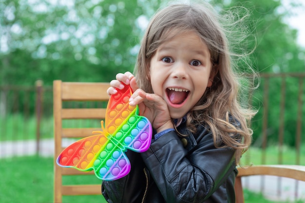 Photo caucasian little girl playing with pop it silicone trendy rainbow colow toy