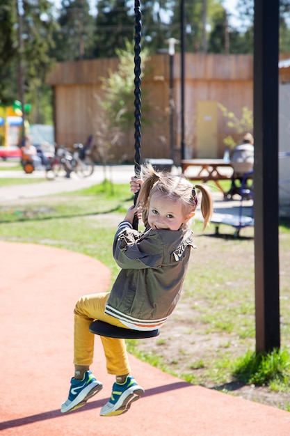 Caucasian little girl rides a bungee swing on the playground and smiles outdoors on a sunny day.