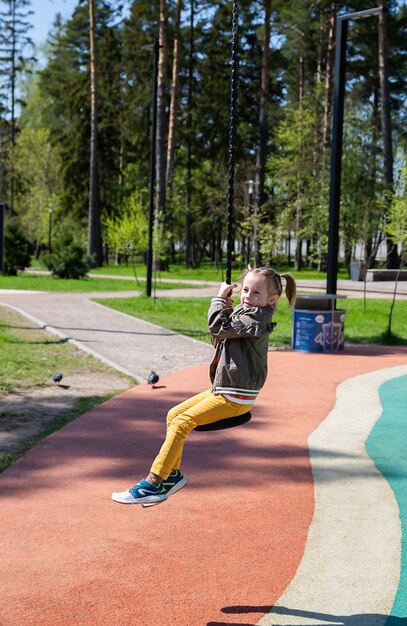 Caucasian little girl rides a bungee swing on the playground and smiles outdoors on a sunny day.