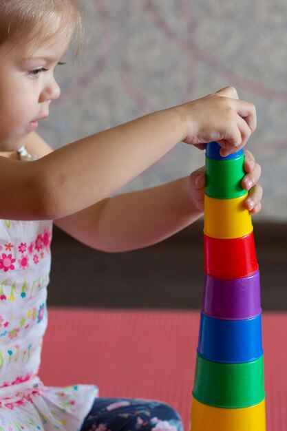 Caucasian little girl of three years old building pyramid using colorful stacking cups