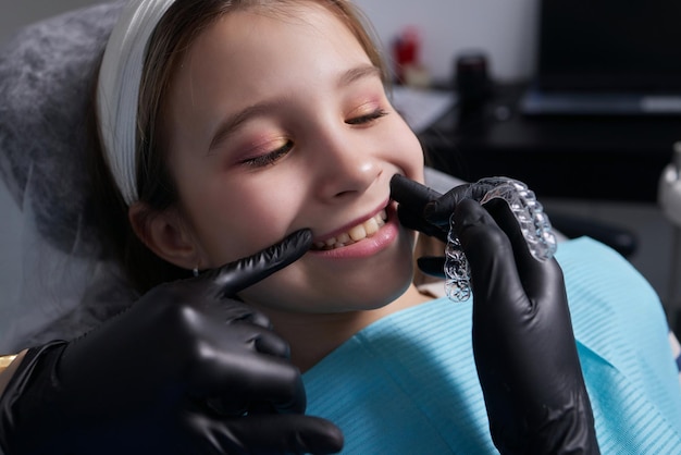 Caucasian little kid girl invisible aligner and pointing to her perfect straight teeth. Dental healthcare and confidence concept.