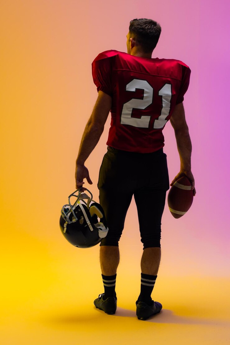 Photo caucasian male american football player holding helmet and ball with neon yellow and purple lighting
