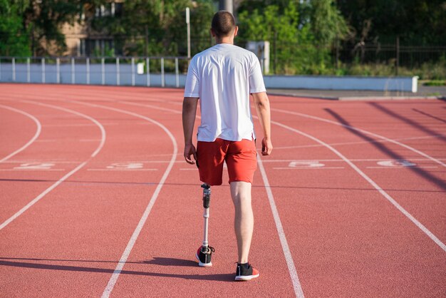 Caucasian male athlete with a prosthesis on his leg walking on\
the track at the stadium. back view. sport concept.