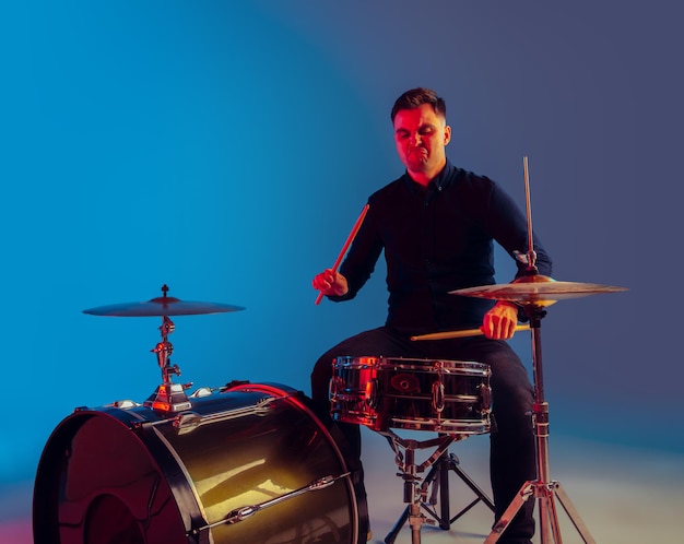 Caucasian male drummer improvising isolated on blue studio background in neon light