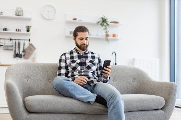 Caucasian male holding smartphone while staying in modern workplace at home