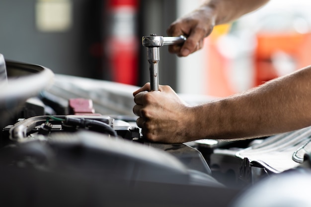 Caucasian male mechanic repairs car in garage. Car maintenance and auto service garage concept. Closeup hand and spanner.