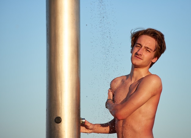 A caucasian male taking a shower at a beach during the day